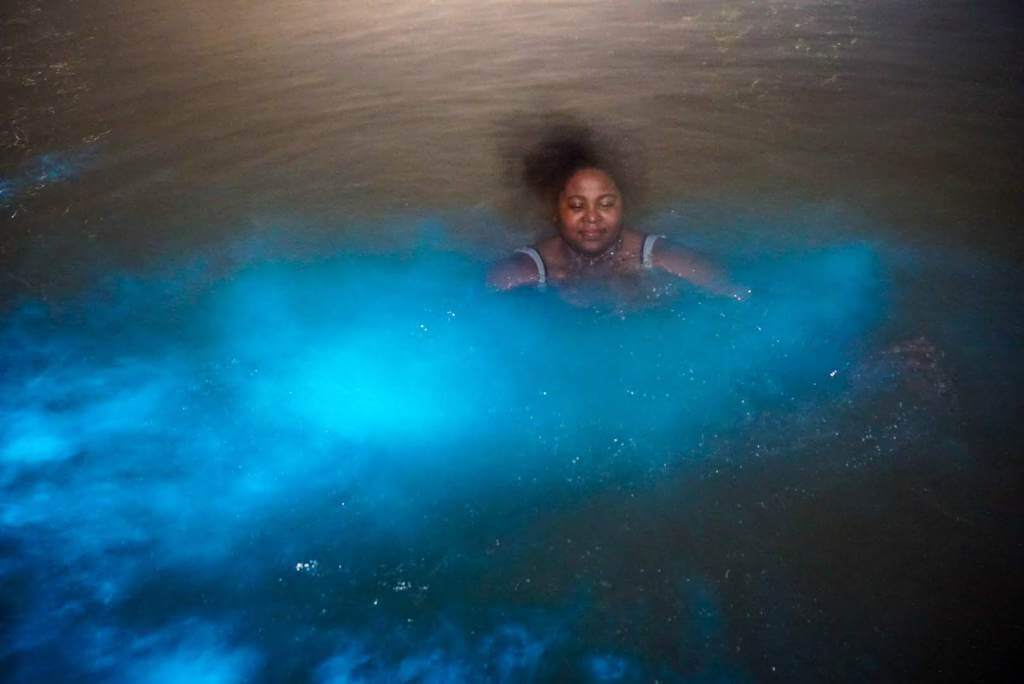black girl swimming in luminous lagoon in Falmouth Jamaica. display bio-luminescence in the world.