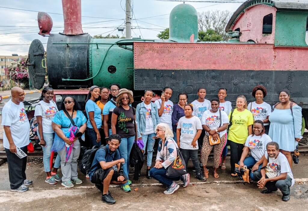 Group of black people pose by an old steam engine train in Trench Town, Downtown Kingston