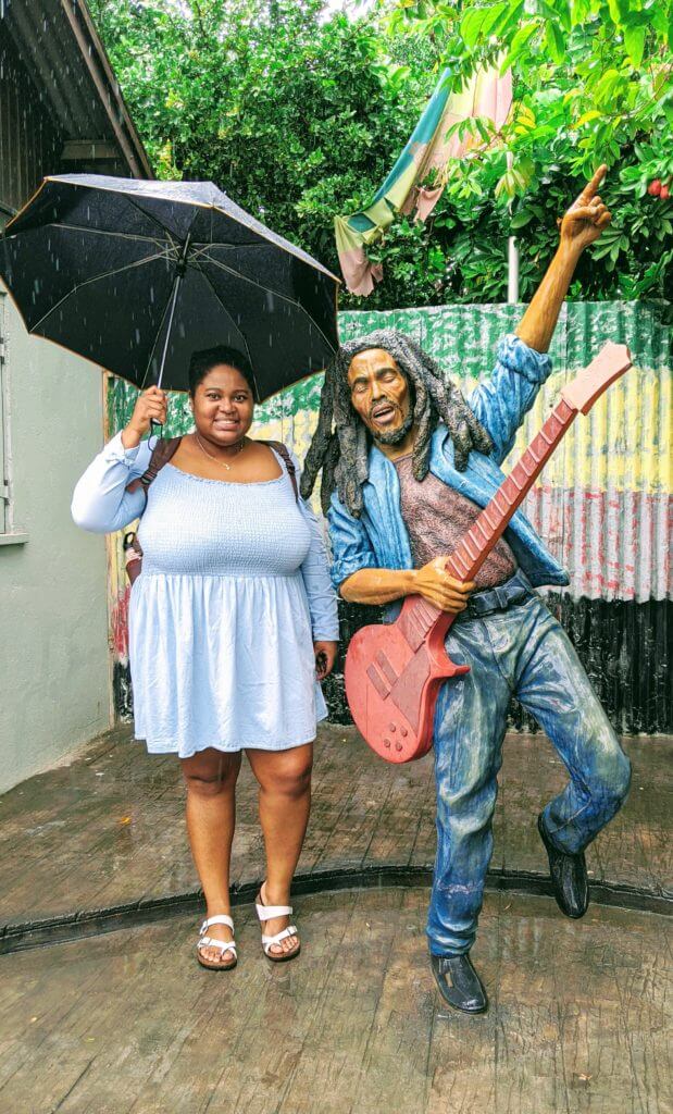 Black curvy woman pose with Bob Marley Statue at Trench Town Culture Yard