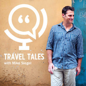 photo of Mike Siegel from Travel Tales Podcast posing on a wall in a blue plaid shirt