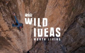 Wild ideas travel podcast to soothe your wanderlust. Man rock climbing in blue outdoor gear.