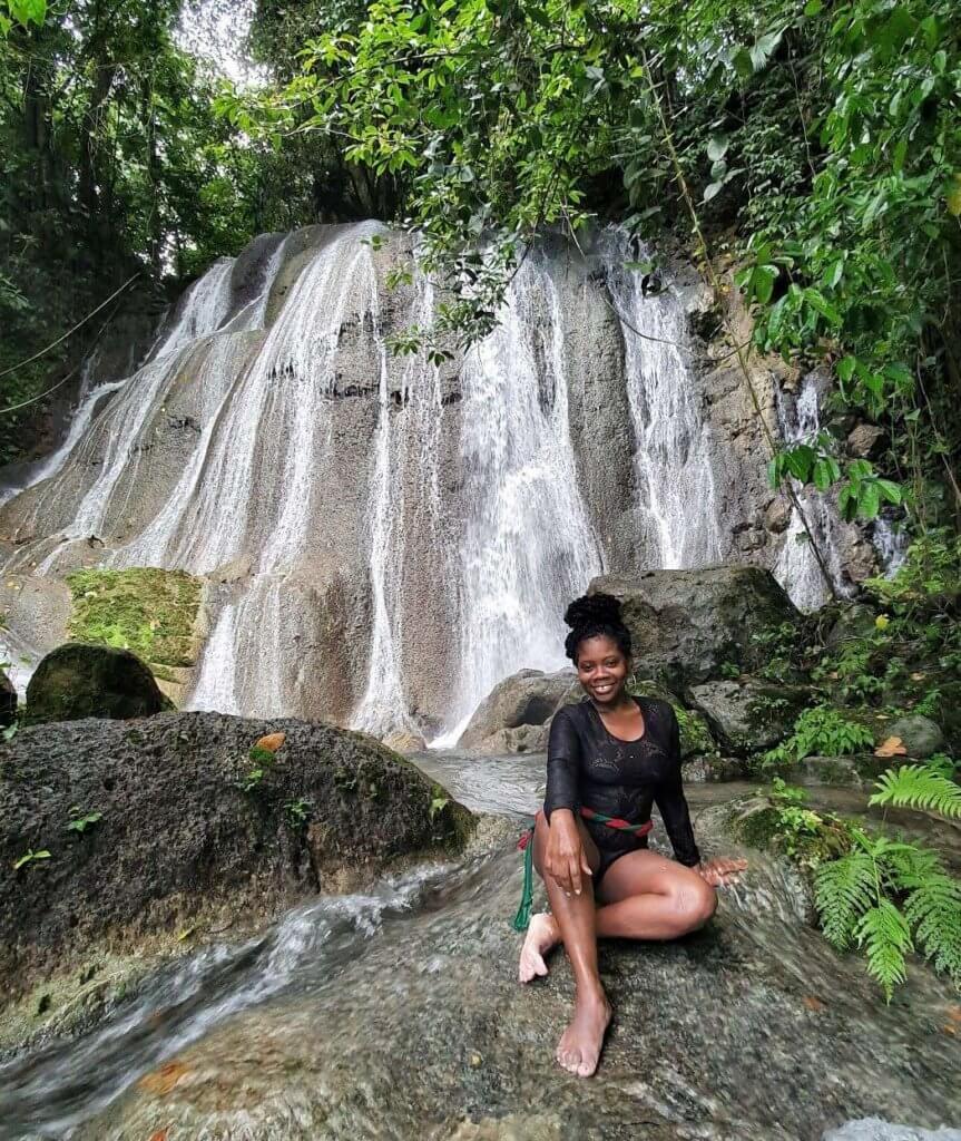 yemalla, travel blogger of natures sweet escapes pose on a rock by a waterfall in jamaica